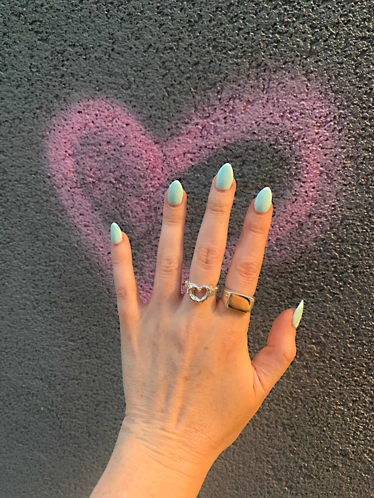 Heart Ring in recycled sterling silver and signet ring, worn on hand in front of pink graffiti heart on gray wall – Black Heart Jewelers