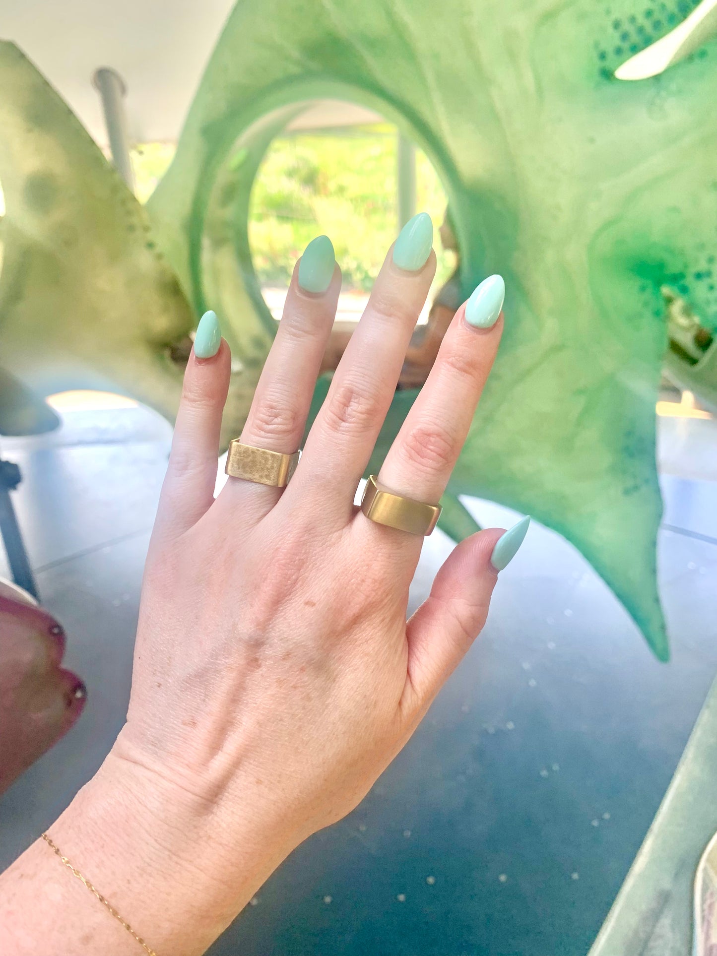 Pyramid Ring and Square Band Ring in eco-friendly brass, worn on hand outdoors against green sculptural backdrop – Black Heart Jewelers